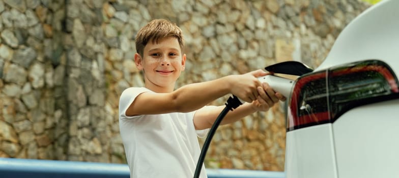 Little boy recharging eco-friendly electric car from EV charging station. EV car road trip travel concept for alternative transportation powered by clean renewable and sustainable energy. Perpetual