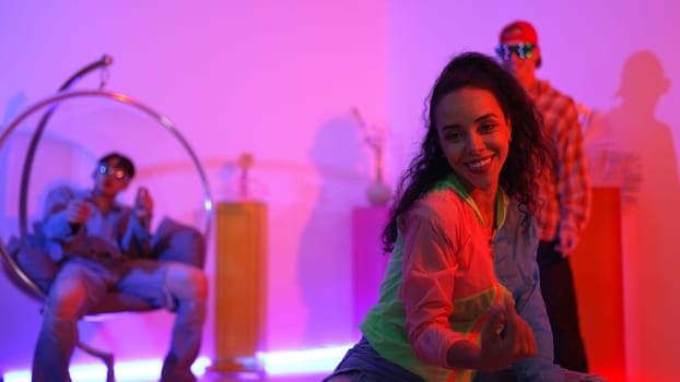 Attractive happy dancer looking at camera while smart woman moving at rhyme with neon light. Professional hispanic performer break dancing while wearing colorful cloth with diverse friend. Regalement.