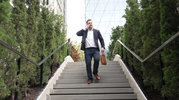 Happy businessman walking down stair and calling manager by using smart phone. Top view of manager talking marketing team and planning financial strategy by telephone while going down stair. Urbane.