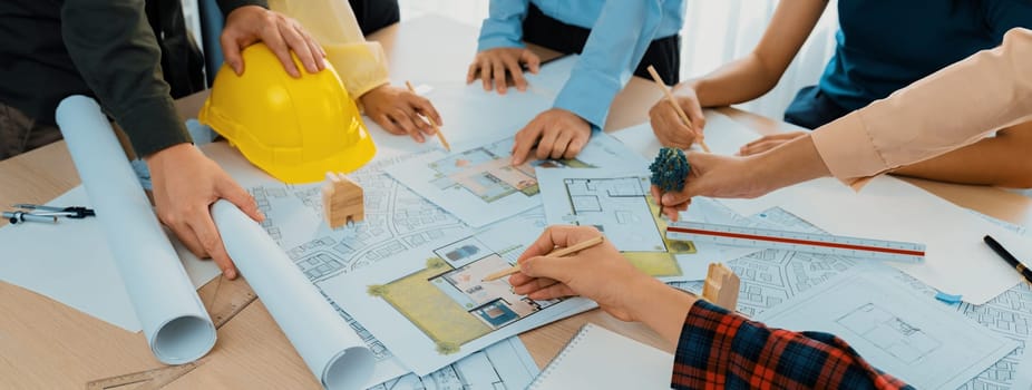 Professional architect cooperate with engineer discussing the use of green design in eco house project on table with blueprint and architectural equipment scatter around. Closeup. Delineation.