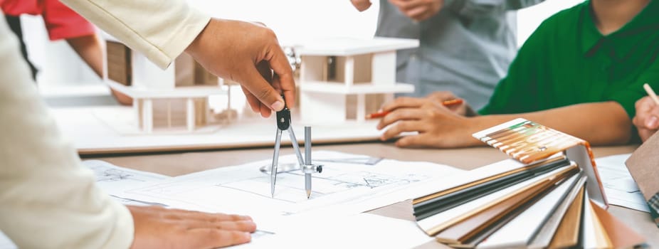 Professional architect team select sustainable house materials while skilled engineer using divider measure blueprint with house model and color palette placed on meeting table. Closeup. Variegated.