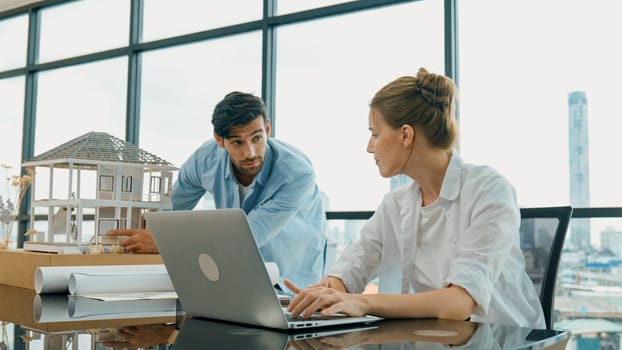 Smart architect engineer inspect house model while colleague using laptop analysis data. Professional designer team working together to design house model construction at modern office. Tracery