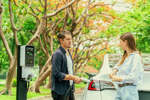 Lovely young couple recharging battery for electric car during autumnal road trip travel EV car in autumnal forest. Eco friendly travel on vacation during autumn. Exalt