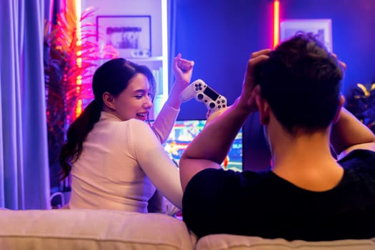 Smiling beautiful woman winner fighting gamer on video game beside loser man at back side. Couple joyful of player on TV using joysticks in studio room in red blue neon light at home place. Postulate.