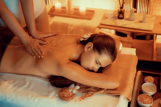 Woman customer having exfoliation treatment in luxury spa salon with warmth candle light ambient. Salt scrub beauty treatment in Health spa body scrub. Quiescent