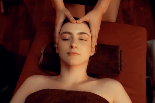 Caucasian woman enjoying relaxing anti-stress head massage and pampering facial beauty skin recreation leisure in warm candle lighting ambient salon spa in luxury resort or hotel. Quiescent