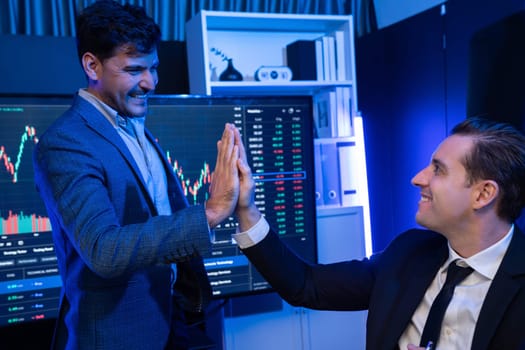 Two stock exchange traders making high five for successful in high profit chart investment at night time. Businessman partners in stock market on stock background in neon light at workplace. Sellable.