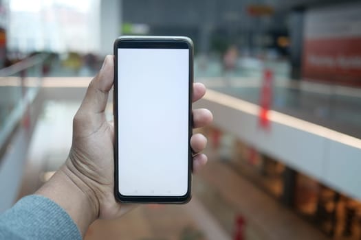 holding smart phone with empty screen against shopping mall background .