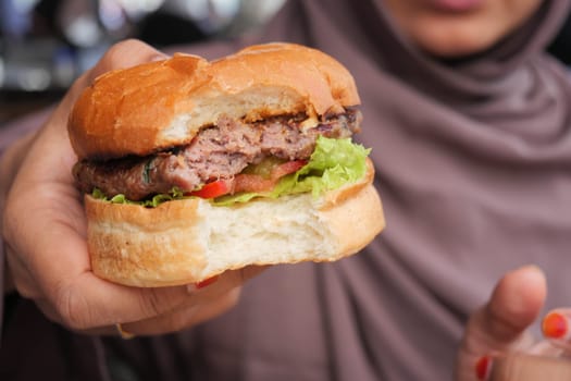 hand holding beef burger on table close up .