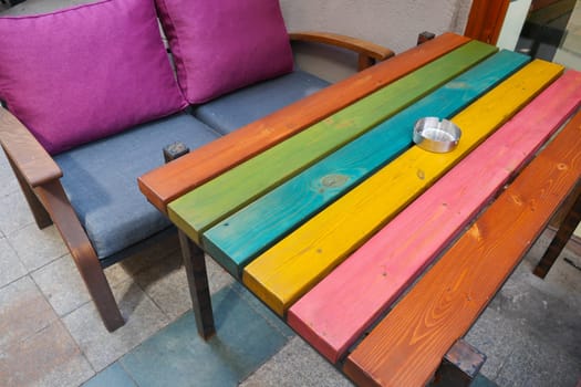 Rainbow wooden table outdoors with ashtray, hardwood and wood stain.