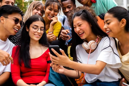 Multiracial group of teen friends looking at phone together outdoors. Social media concept.
