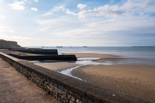 Beach and seawall blue sky and clouds. Sand, sea, ocean and sun. Normandy village of Gold Beach France. Tourism. High quality photo