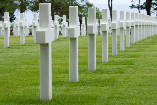 American cemetery at Normandy area. WWII memorial. Lines of grave stones with arch over landscape. Trees in background. High quality photo