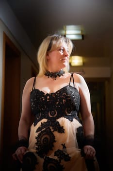 Full length view of a blonde female model, dressed in a black and white queen dress in dark corridor. Mysterious stranger alone inside castle or hotel