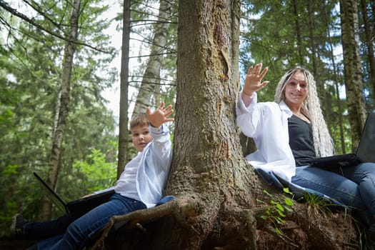 Mother and son with a laptops in the forest in summer. Fat young smart teenage boy and woman working with modern IT technologies in nature