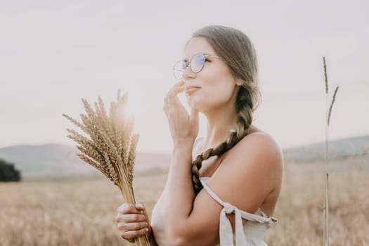 A woman is holding a bunch of wheat in her arms. The wheat is dry and brown, and the woman is wearing a white dress. The scene is set in a field, and the woman is posing for a photo