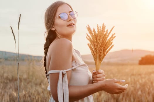 A woman is holding a bunch of wheat in her arms. The wheat is dry and brown, and the woman is wearing a white dress. The scene is set in a field, and the woman is posing for a photo