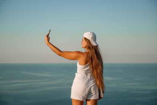 Selfie woman in a cap, white tank top and shorts makes a selfie shot mobile phone post photo social network outdoors on the background of the sea beach people vacation lifestyle travel concept