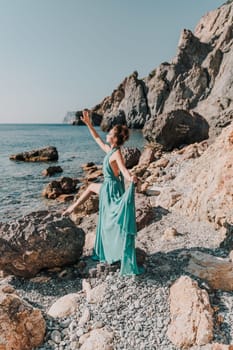 Woman green dress sea. Woman in a long mint dress posing on a beach with rocks on sunny day. Girl on the nature on blue sky background