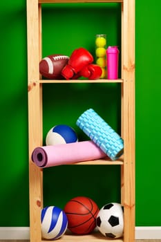 Shelves with different sports equipment against green wall close up