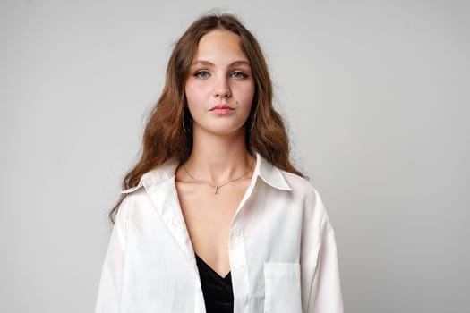 A woman with flowing long hair is seen wearing a crisp white shirt in this portrait. Her hair cascades down her back as she looks directly at the camera.