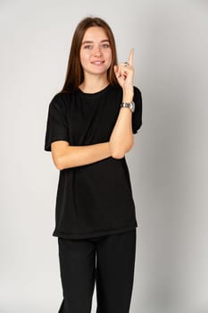 Smiling Young Woman Pointing to Copy Space Against a Grey Background in Studio