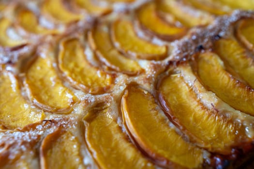 A close up of a dessert made of sliced peach. The dessert is covered in a caramel glaze and has a golden brown crust. The peach are arranged in a spiral pattern, creating a visually appealing.