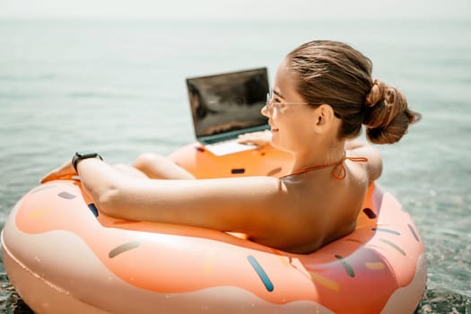 Woman laptop sea. Freelancer woman in sunglases floating on an inflatable big pink donut with a laptop in the sea. People summer vacation rest lifestyle concept