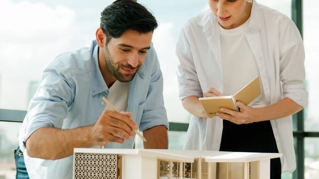 Skilled architect engineer team discussion about house model construction. Smart interior designer sharing, talking about building design while beautiful coworker taking a note. Design. Tracery