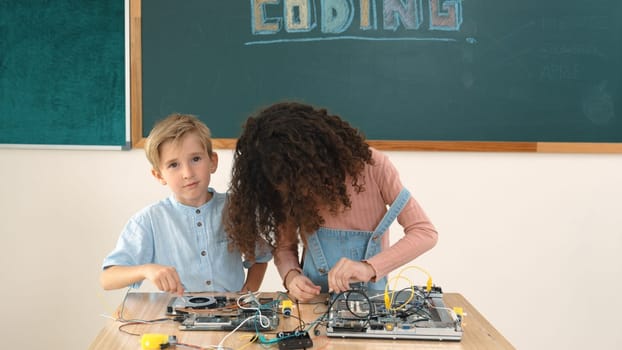 Smart girl standing while fixing electronic board by using screwdriver. Happy student and happy caucasian boy working together to inspect electric system. Curious children working on board. Pedagogy.