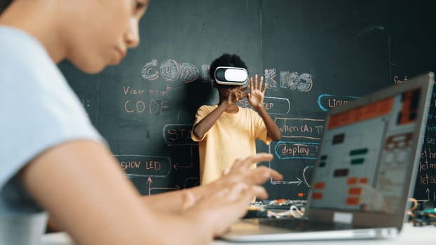 Closeup of school girl hand coding program while african student using VR interact with metaworld. Smart boy wearing virtual reality glasses and playing video games at innovative class. Edification.