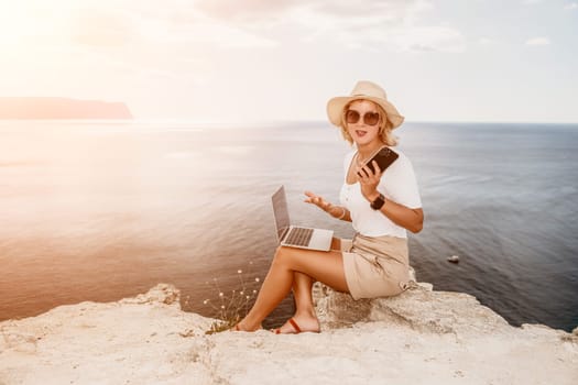 Digital nomad, Business woman working on laptop by the sea. Pretty lady typing on computer by the sea at sunset, makes a business transaction online from a distance. Freelance remote work on vacation