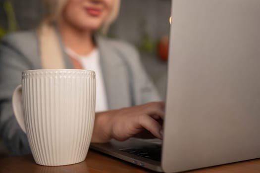 A woman is typing on a laptop while holding a white coffee cup. Concept of productivity and focus, as the woman is likely working on a project or task