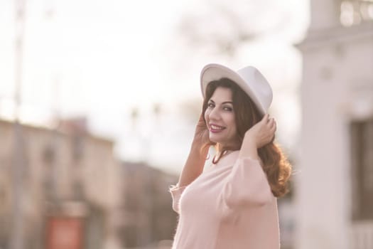 A woman wearing a white hat and a pink shirt is smiling and posing for a picture. The image has a warm and cheerful mood, with the woman's smile and the bright colors of her outfit