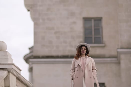 woman in elegant coat and hat against an intricate architectural backdrop, harmoniously blending modern fashion with historical allure. The soft daylight adds to its timeless appeal