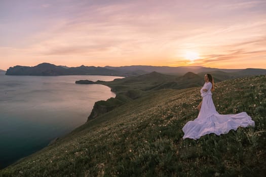 A woman in a white dress stands on a hill overlooking a body of water. The scene is serene and peaceful, with the sun setting in the background. The woman is enjoying the view