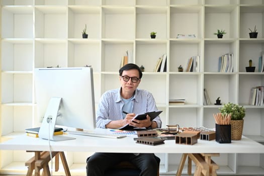 Portrait of experienced senior male architect sitting in the modern office.