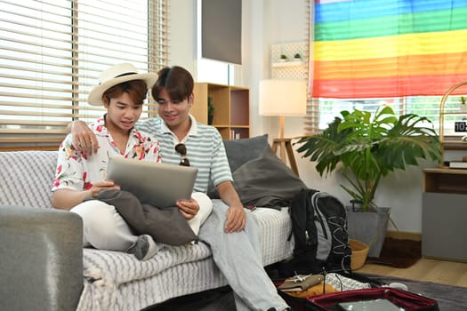 Cheerful asian gay couple booking hotel reservation on laptop preparing for vacation trip.
