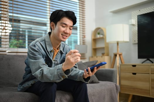 Handsome asian man holding a credit card and purchasing online on smartphone.