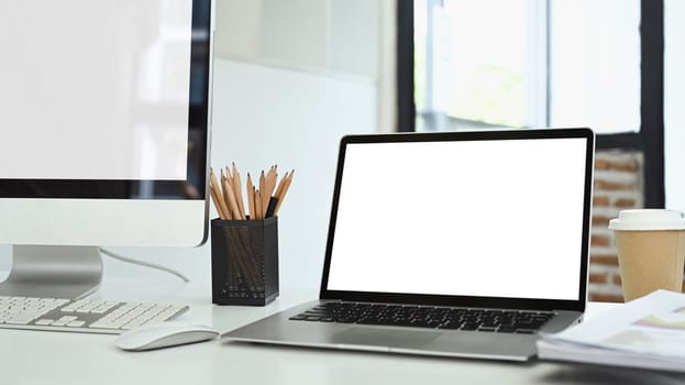 Laptop computer with blank screen, documents and stationery on white office desk.