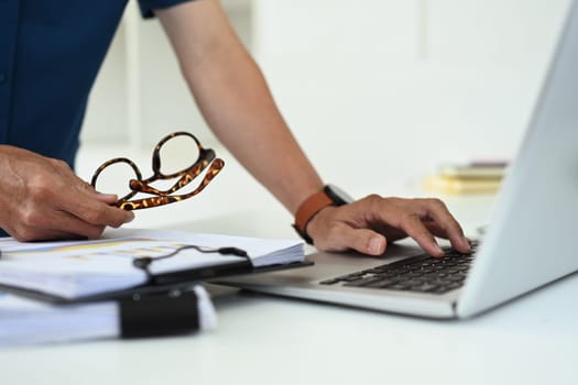 Cropped shot of businessman holding eyeglasses using laptop at office desk.