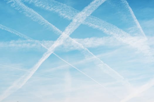 Airplane condensation trail or contrail with lines of clouds over blue sky background. Travel concept