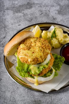 Double fish burger with potato salad on a metal plate