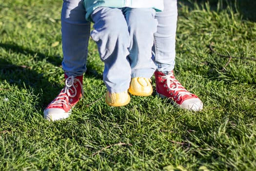 A person wearing jeans stood beside a child sporting red sneakers on their feet, showcasing a contrast in footwear choices