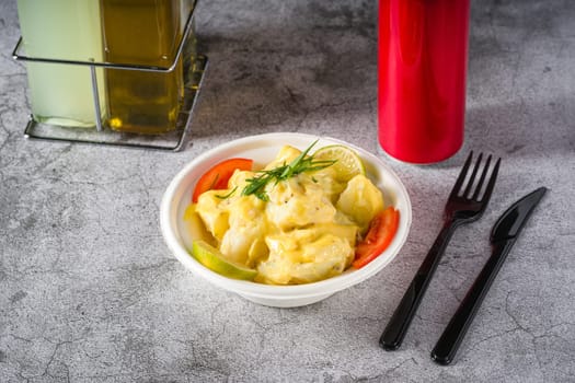 Potato salad with tomatoes and lemon on gray stone table