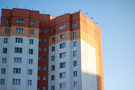 In the backdrop of a blue sky stands a towering building, showcasing urban design and composite material. The facade of the condominium reflects the azure sky in the cityscape