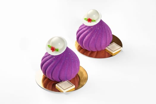 Chic velvety purple mousse desserts in shape of swirls topped by white chocolate hats, displayed on golden cardboards against white background