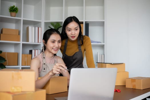 Couple of young Asian women running a small business together selling products online using laptops.