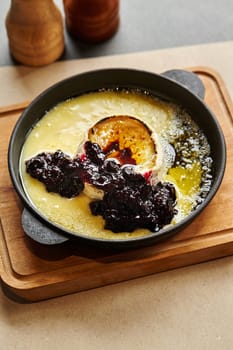 Warm baked Camembert cheese oozing in cast iron skillet served on wooden board, paired perfectly with dollop of homemade currant jam for sweet and savory treat