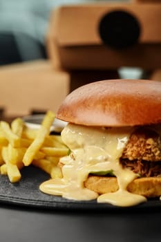 Juicy chicken burger in glossy browned bun with generous helping of melting cheese sauce, crispy fried onions and side of golden fries, ready for quick takeaway